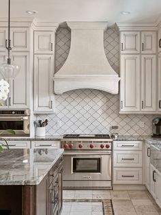 a kitchen with white cabinets and marble counter tops, an oven hood over the stove