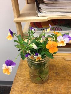 a jar filled with flowers sitting on top of a wooden table next to a stack of books