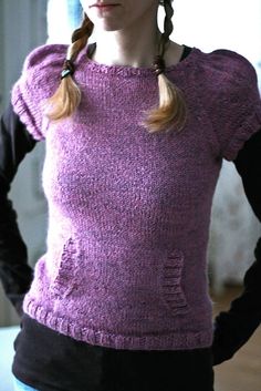 a woman standing with her hands on her hips wearing a purple sweater and black pants