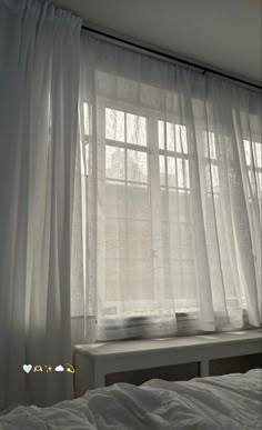 a bed sitting under a window covered in white curtains