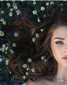 a woman laying on top of a field of flowers next to blue and yellow daisies