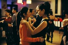 two young women dancing together in a dance hall with other people standing around and looking at each other