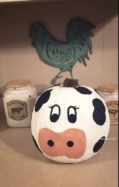 a painted pumpkin sitting on top of a counter next to jars and a rooster figurine