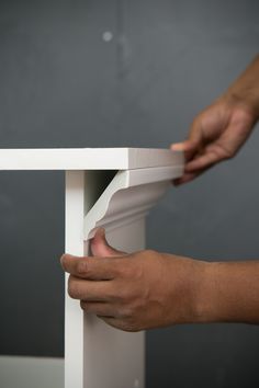 a person is holding the edge of a white table with one hand and another hand reaching for it