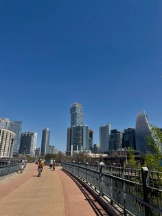 people riding bikes on a bridge in the city with tall buildings behind them and blue sky