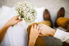 the bride and groom hold hands as they sit next to each other with flowers in their lap