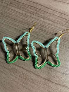 two green and gold beaded earrings on top of a wooden table