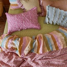 an unmade bed with many pillows and blankets on top of it, all in different colors