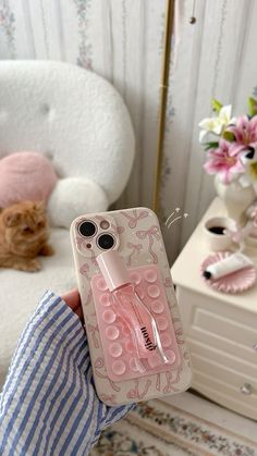 a person holding an iphone case with a pink perfume bottle on it and flowers in the background