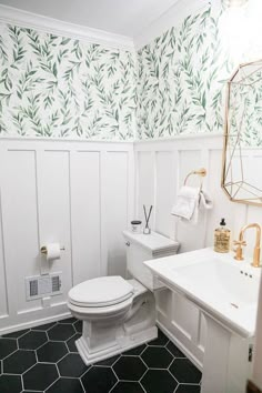 a white toilet sitting next to a sink in a bathroom under a mirror with green leaves on it