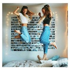 two girls jumping on a bed with their arms in the air and one girl is wearing jeans