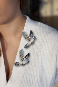 a close up of a woman wearing a white sweater and two birds broochies