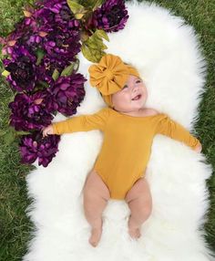 a baby laying on top of a white rug next to purple flowers