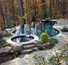 an outdoor swimming pool surrounded by rocks and trees in the fall season, with water flowing from it