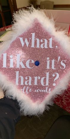 a pink and white graduation cap that says what like it's hard?