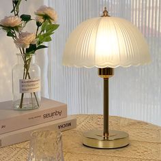 a glass vase with flowers in it sitting on a table next to a book and lamp