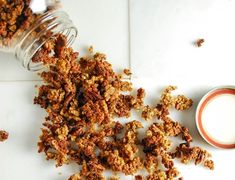 granola next to a glass of milk on a white counter top with scattered granola