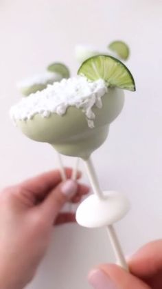 a person is holding a green drink with limes and whipped cream on it,