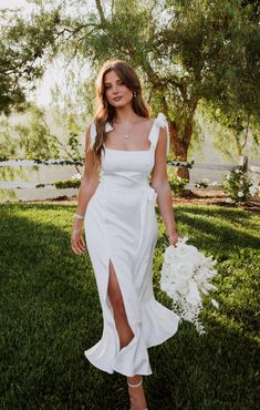 a woman in a white dress holding a bouquet and posing for the camera with her hand on her hip