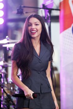 a woman holding a microphone in her right hand while standing next to a drum set