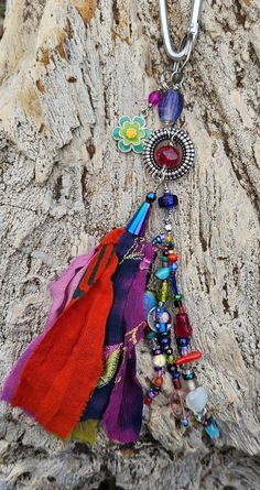 a multicolored necklace is hanging on a tree trunk with beads and other items