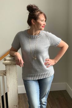 a woman standing in front of a stair railing wearing jeans and a sweater with an open back