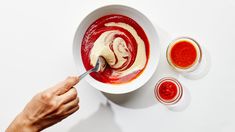 a person holding a spoon in a bowl of food with sauces on the side