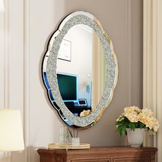 a mirror sitting on top of a wooden dresser next to a vase filled with flowers