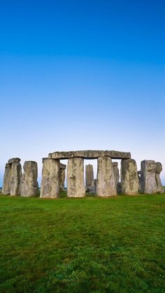 stonehenge in the middle of a grassy field with blue skies above it and green grass below