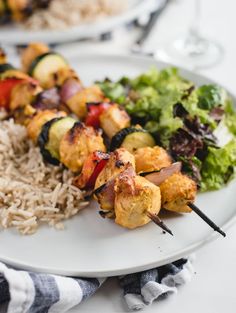 a white plate topped with meat and veggies on skewers next to rice