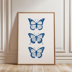 three blue butterflies on a white wall above a wooden floor