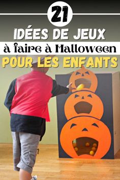 a young boy is playing with an orange pumpkin in front of a cardboard box that has faces on it