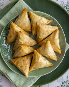 a green plate topped with triangular pastries on top of a white and green table cloth