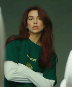 a woman with long red hair wearing a green shirt and white gloves looking at the camera