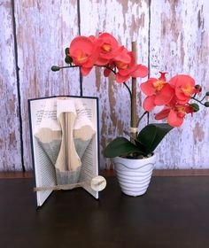 an open book with flowers in it next to a vase filled with red orchids