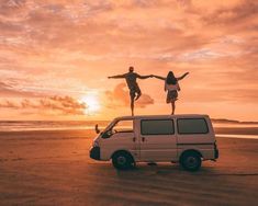 two people standing on top of a van in front of the ocean with their arms outstretched