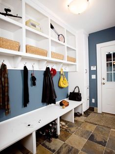 a white bench sitting next to a wall filled with coats and purses on top of it