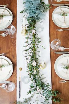 the table is set with white plates, silverware and greenery