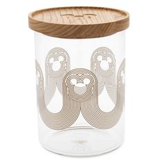 a clear glass jar with wooden lid and an intricate design on the front, sitting on a white surface