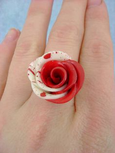 a person's hand with a red and white rose ring on top of it