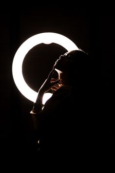 a woman standing in front of a circular light with her hand on her face and looking into the distance