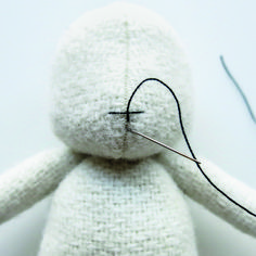 a white teddy bear with a needle in it's mouth and some thread on its nose