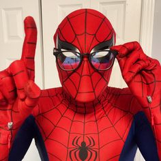 a man in a spiderman costume making the peace sign with his hands and wearing glasses