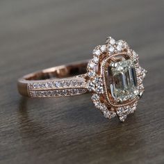 an engagement ring with a large green diamond surrounded by small white and brown diamonds on a wooden surface