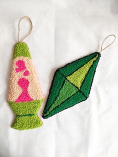 two crocheted ornaments are sitting on a white sheet, one is green and the other is pink