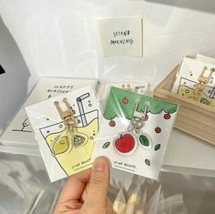 a person holding up two tags in front of some fruit and vegetable themed magnets