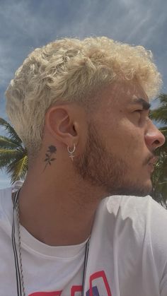 a man with blonde hair wearing a white shirt and silver earrings looking off into the distance