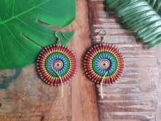 a pair of colorful earrings sitting on top of a wooden table next to a green leaf