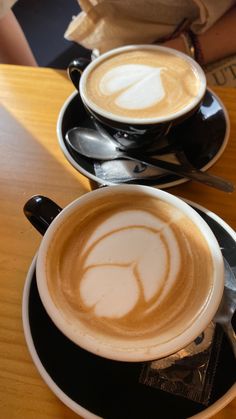 two cups of cappuccino on saucers with spoons