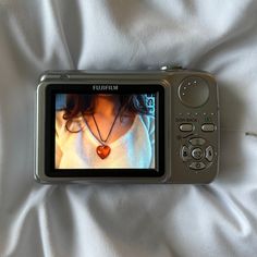 a cell phone is laying on a bed with white sheets and a heart necklace hanging from it's screen